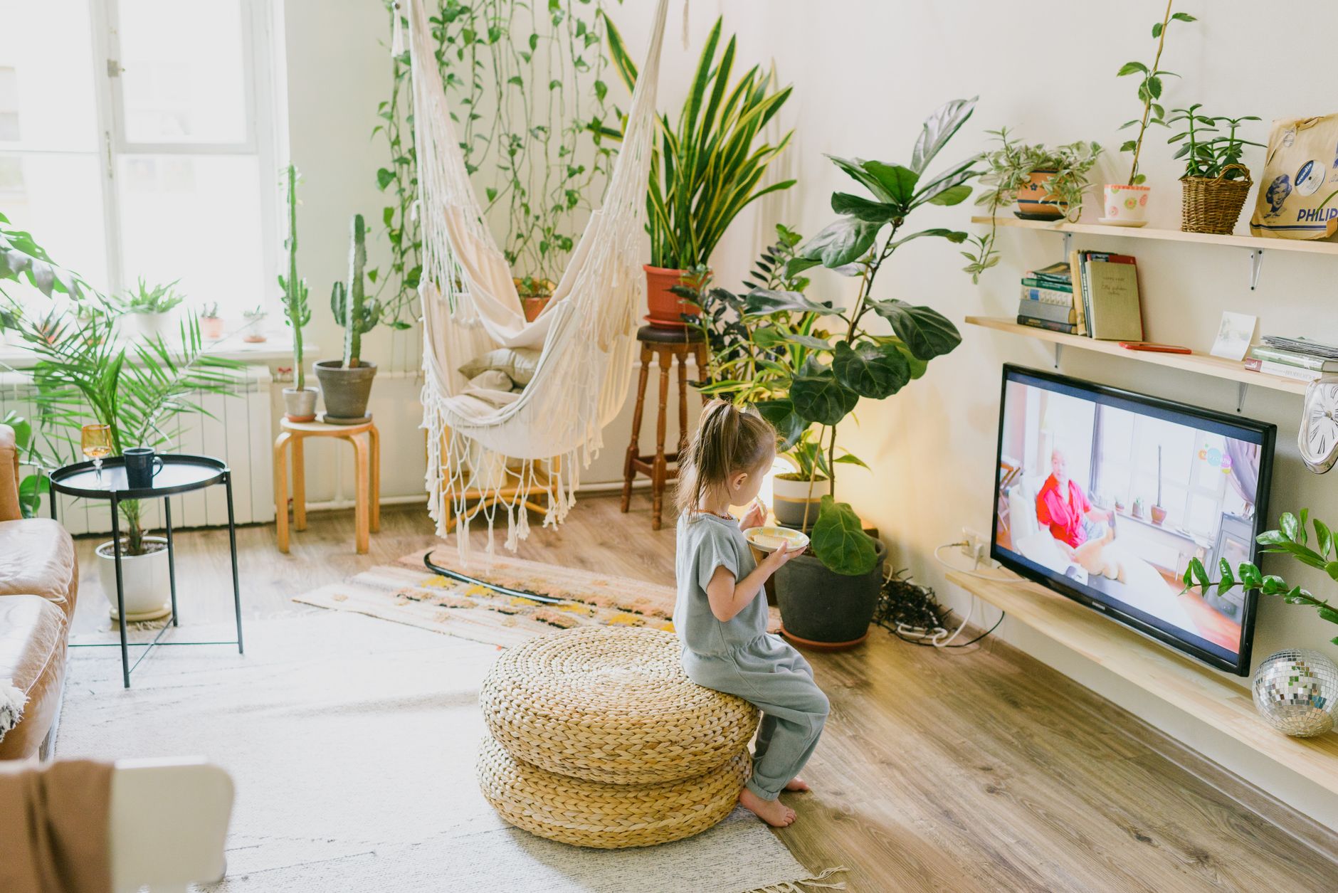 Kind in een woonkamer vol planten met een hangstoel.